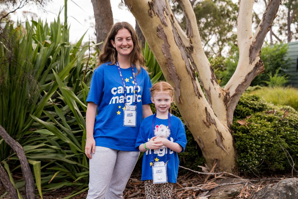 Woman and child standing together smiling wearing blue Camp Magic tshirts